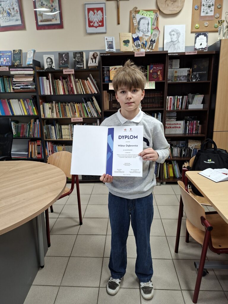 Uczeń prezentuje dyplom na tle szafy bibliotecznej.